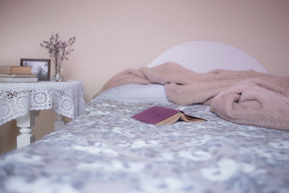 A cozy bedroom interior with a comfortable bed, open book, and lace-covered table for relaxation.