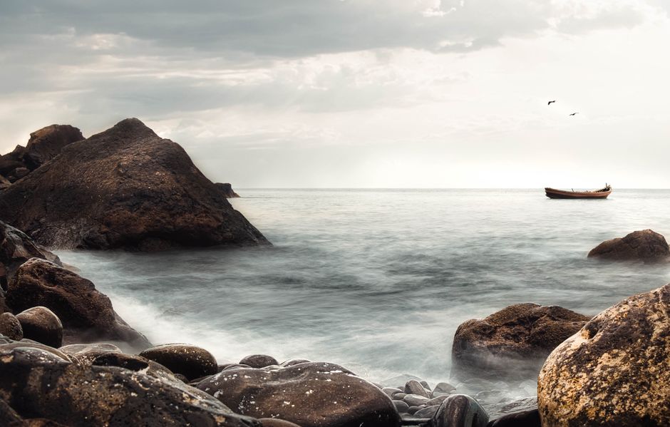 Peaceful seascape at dawn featuring rocks, a distant boat, and a calm sea.