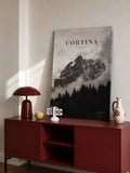 Poster di montagna con cime rocciose scure, conifere e grande titolo CORTINA.