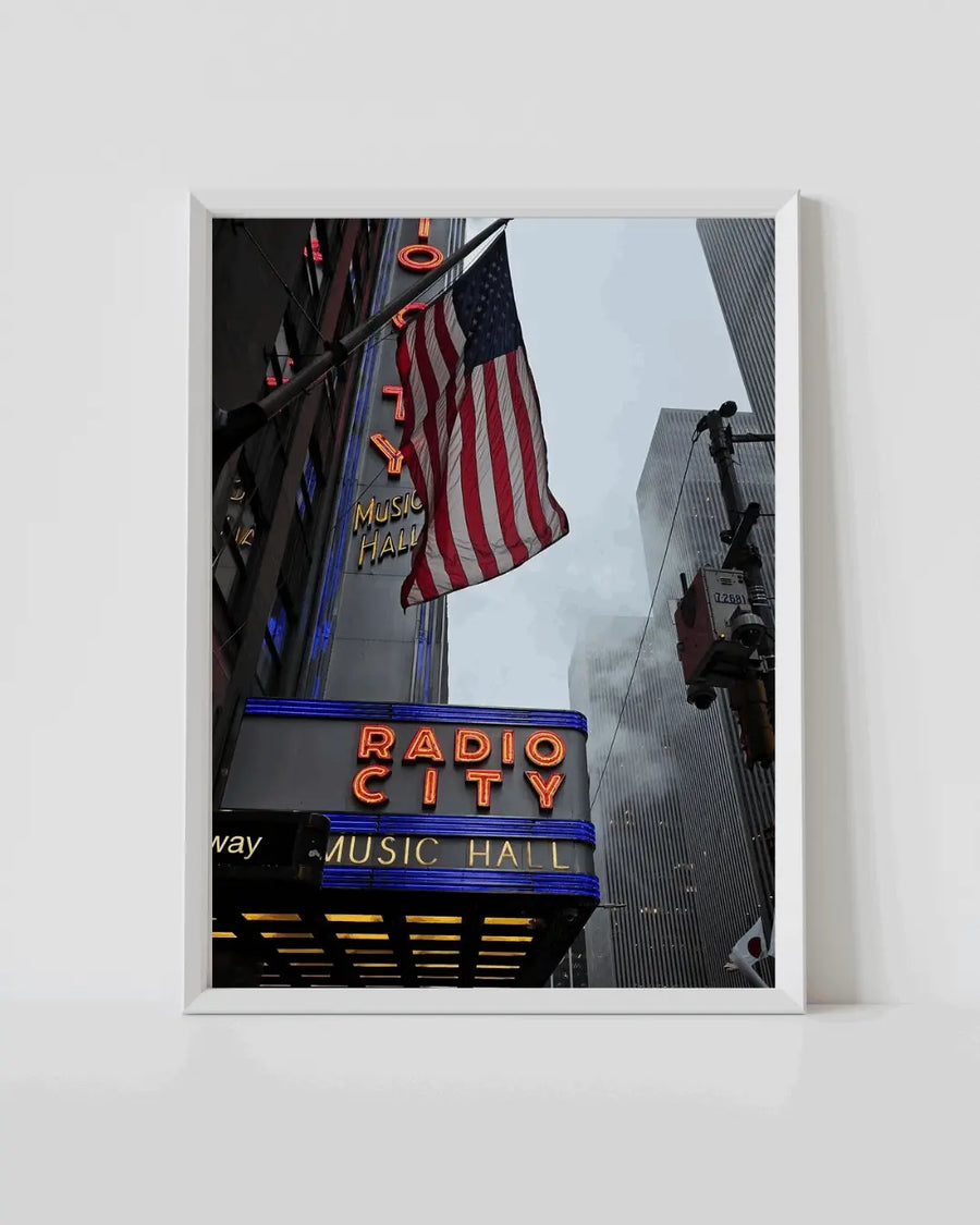 White framed poster with Radio City sign, US flag and street lights