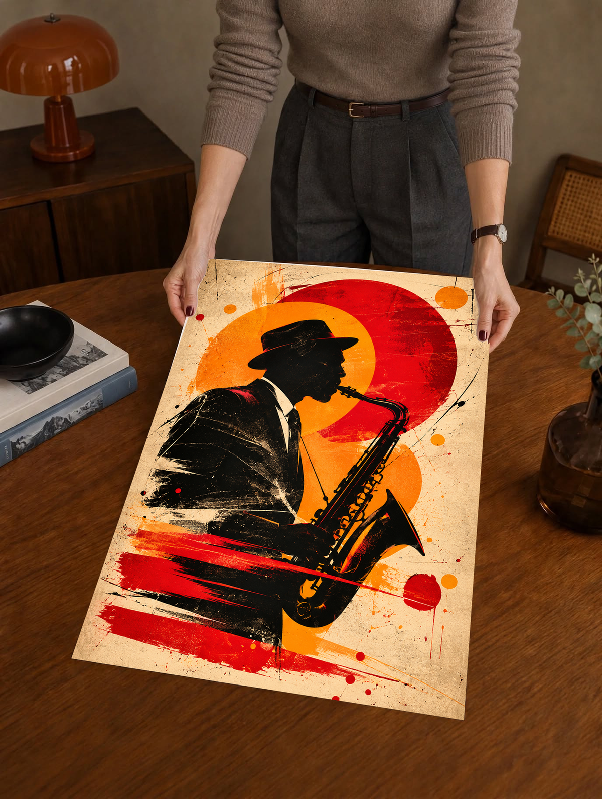 Unframed abstract silhouette poster held by hand, featuring a bold black figure, vivid red circular form and expressive orange and black painted details.