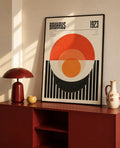 Geometric art print in black frame with red/orange circle and black vertical stripe pattern