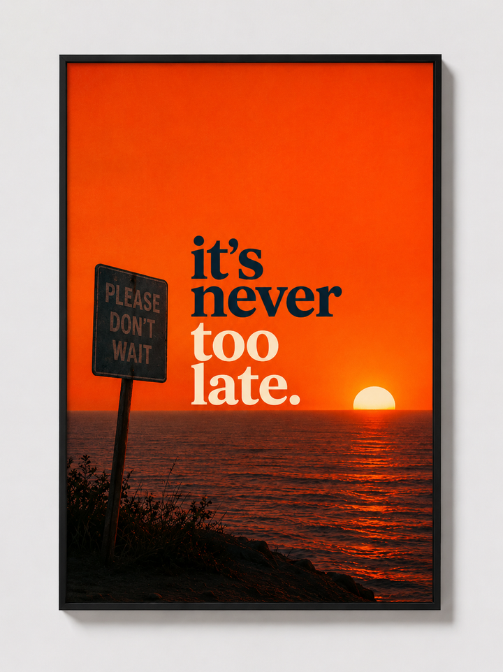 Black-framed motivational wall art with “it’s never too late” over orange sunset sea.