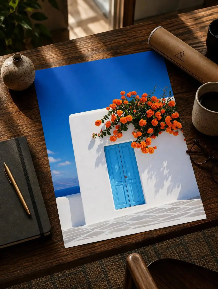 Blue door wall art print with orange flower garland on white facade, angled view