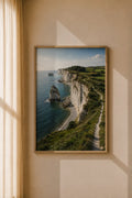 Framed coastal cliff art print in a dark wood frame, ocean, white cliffs, and green fields