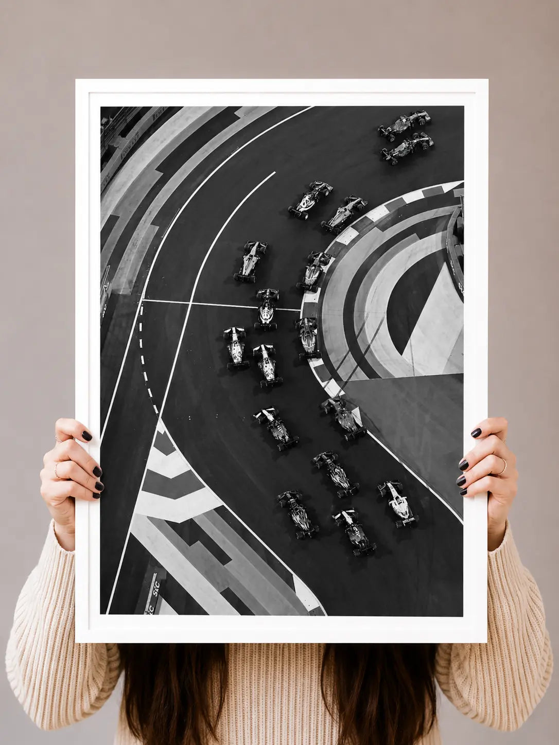Framed black-and-white racing track art print held up, cars on a curved circuit