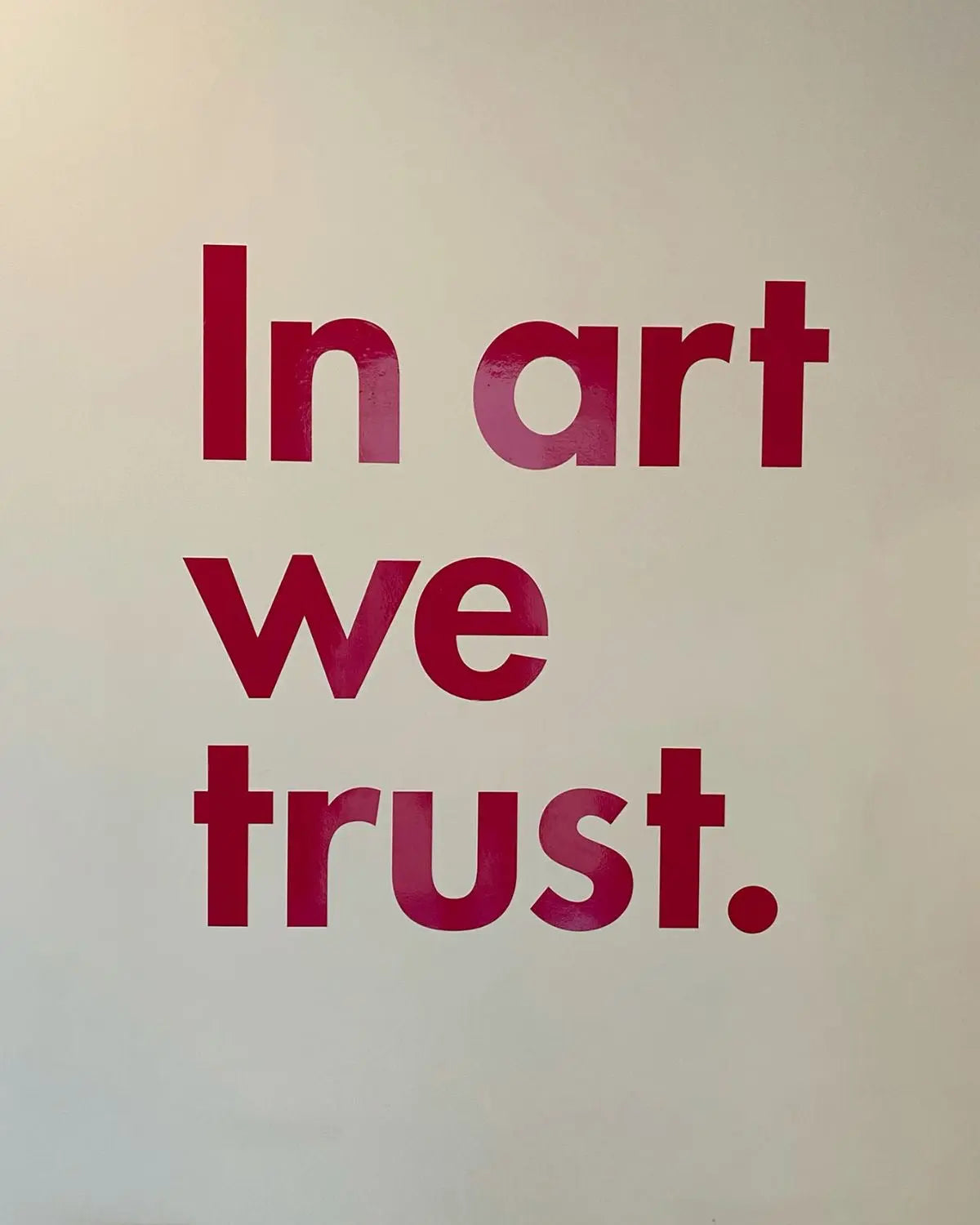 Typography wall print with bold red "In art we trust." text on white background