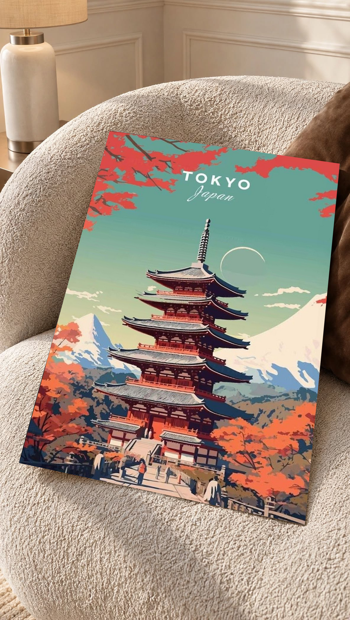 Japanese Pagoda Wall Poster resting on a cream upholstered chair, with orange autumn trees surrounding the tiered red building and Mount Fuji rising beneath Tokyo lettering.
