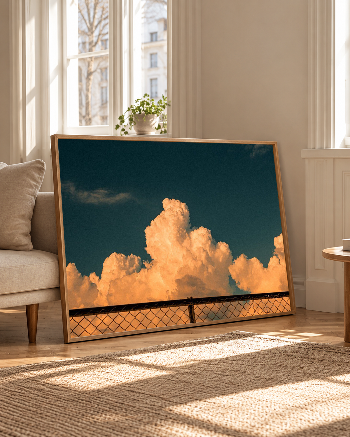 Dramatic cloud wall art positioned on a wooden floor beside a leafy indoor plant, combining copper-colored cloud formations with a deep blue backdrop in a softly lit contemporary room.