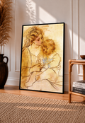 Picasso Mother and Child Print in a black frame leaning against a sunlit wall, showing a seated mother embracing her child in warm ochre tones beside wooden furniture and a woven rug.