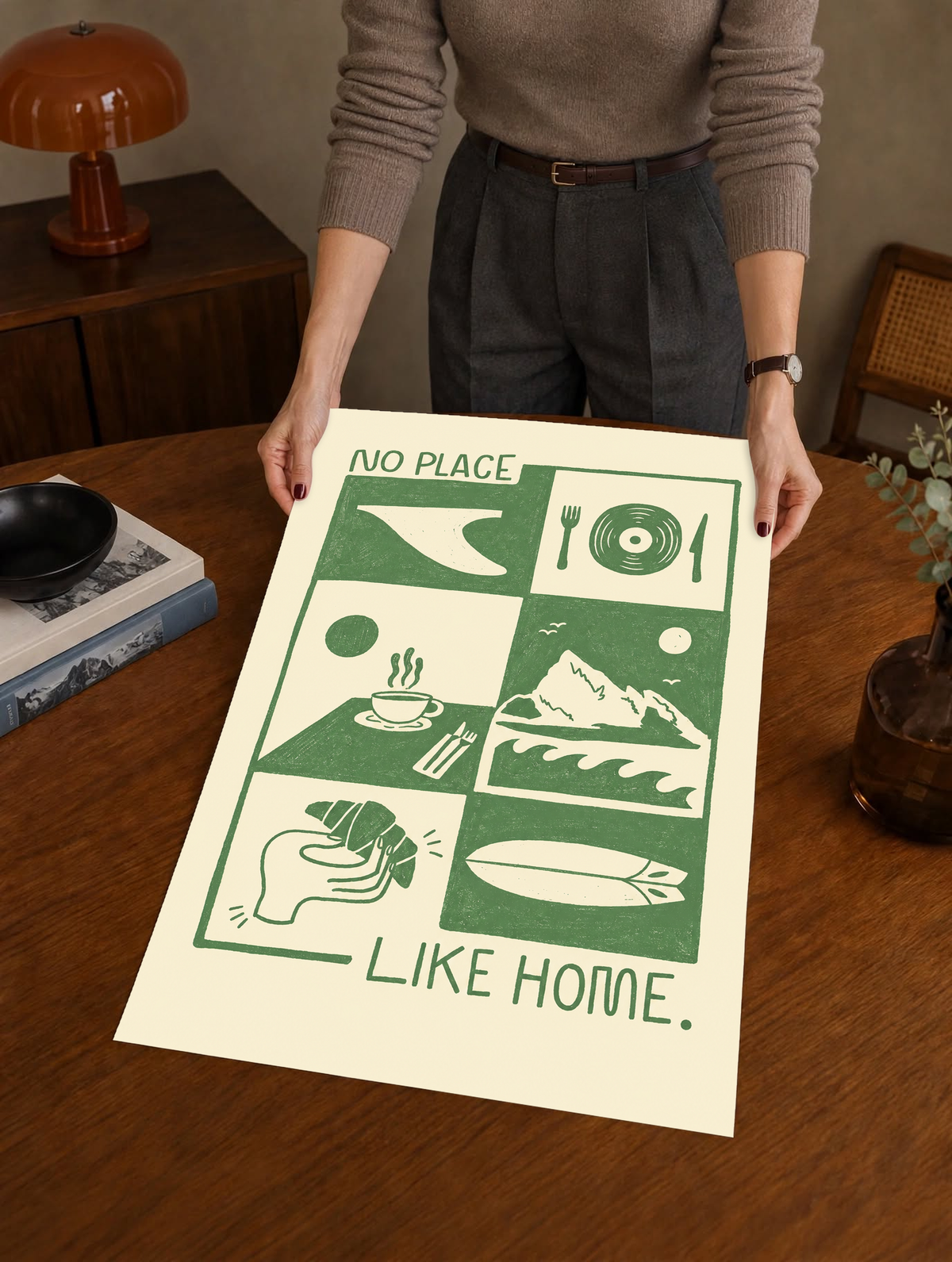 Green-and-cream art print held up: “NO PLACE LIKE HOME” with collage illustration