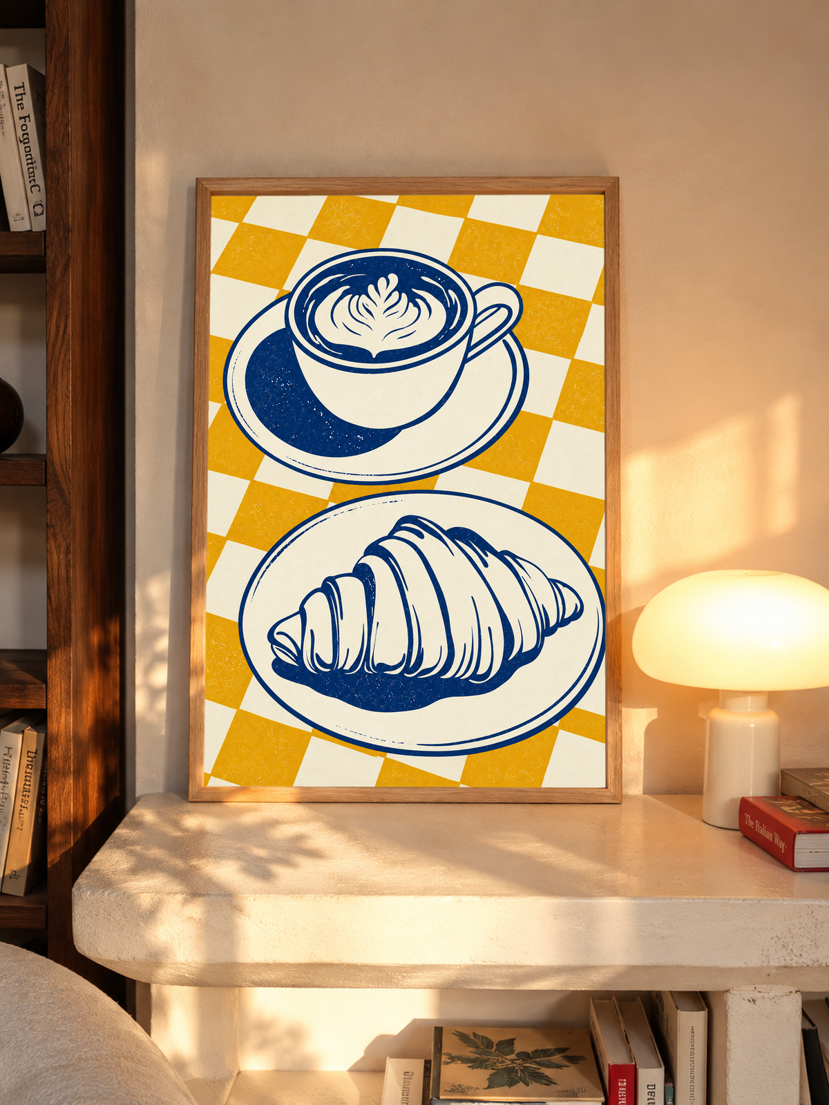 Tazza blu navy con piattino sopra un croissant su un piatto separato, davanti a uno sfondo a quadri senape e crema, in una cornice in rovere su una mensola accanto a una lampada accesa, nella calda luce del sole.