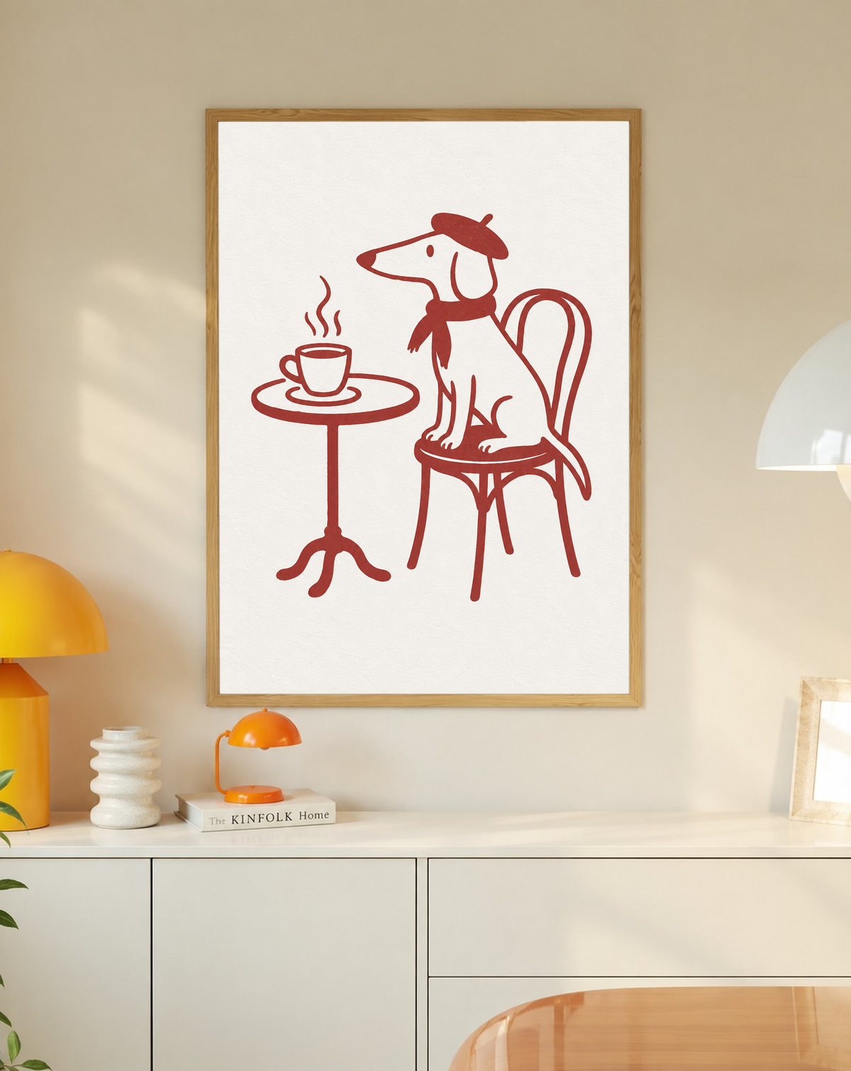 Cane dal muso lungo con basco e sciarpa su una sedia da bistrot, vicino a una tazza fumante e un tavolino rotondo, a linee rosse su crema, in una cornice in rovere sopra un mobile bianco con piccole lampade e oggetti decorativi.