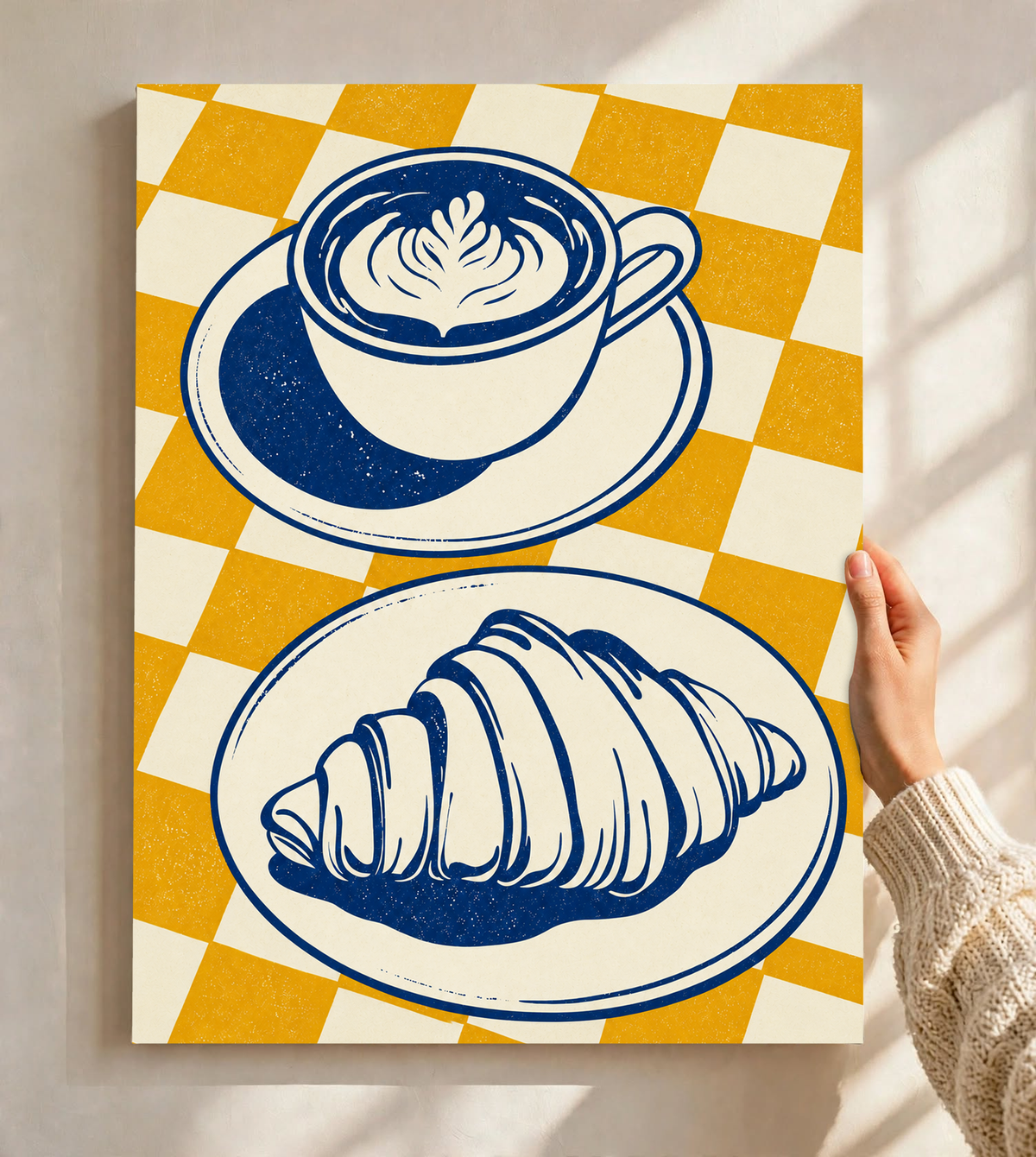 Tazza blu navy con piattino sopra un croissant su un piatto separato, davanti a uno sfondo a quadri senape e crema, come poster senza cornice tenuto contro una parete chiara con morbide ombre della finestra.