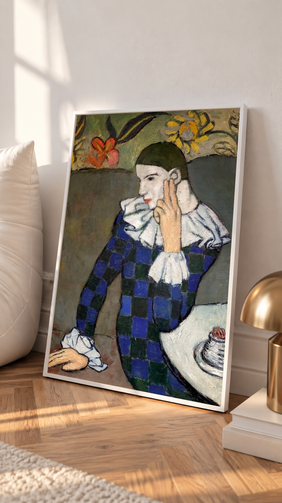 Leaning on a wooden surface against a sunlit wall, the Picasso Seated Harlequin Print shows the pale-faced figure resting fingers against the cheek, with dark blue checks contrasting against white cuffs.