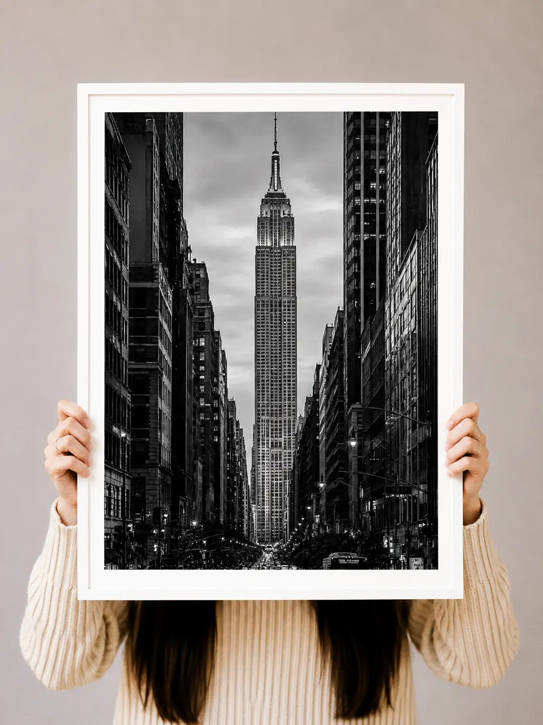 Black-and-white NYC skyline art print in a white frame, held up by two hands