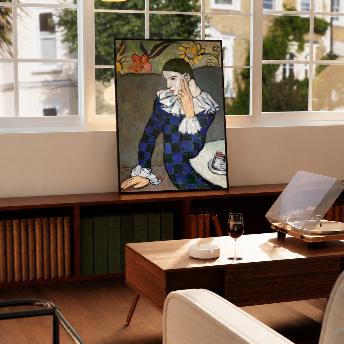 Leaning on a wooden surface against a sunlit wall, the Picasso Seated Harlequin Print shows the pale-faced figure resting fingers against the cheek, with dark blue checks contrasting against white cuffs.