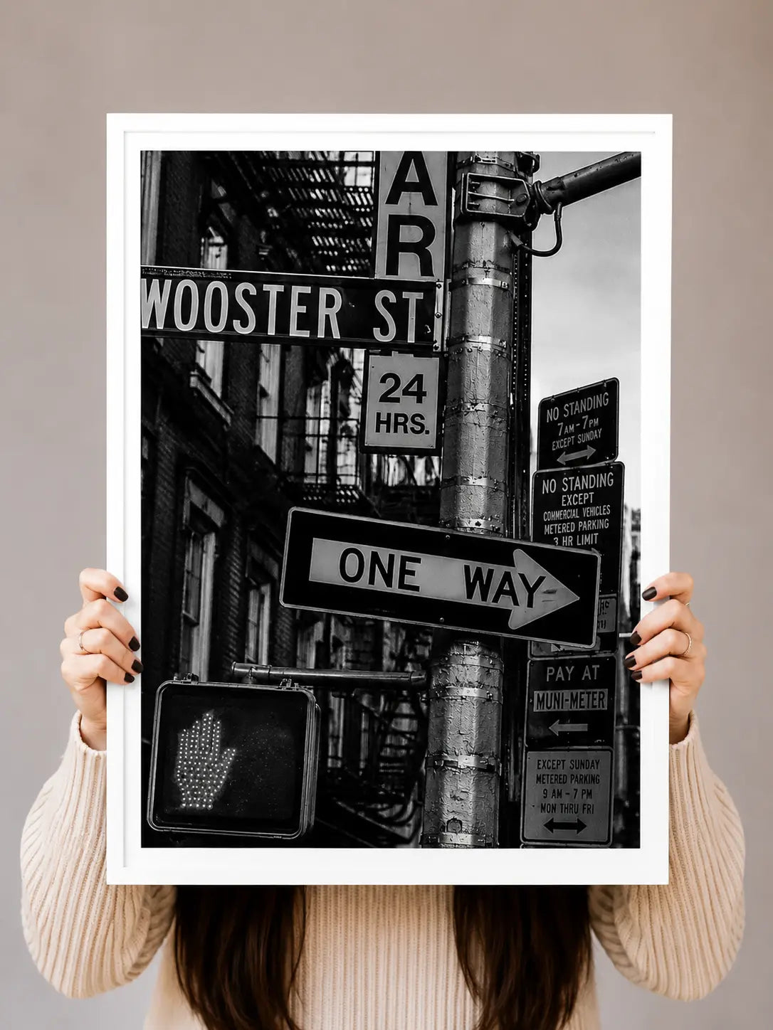 Street sign art print held up, black-and-white signs including “One Way” and “24 HRS”.