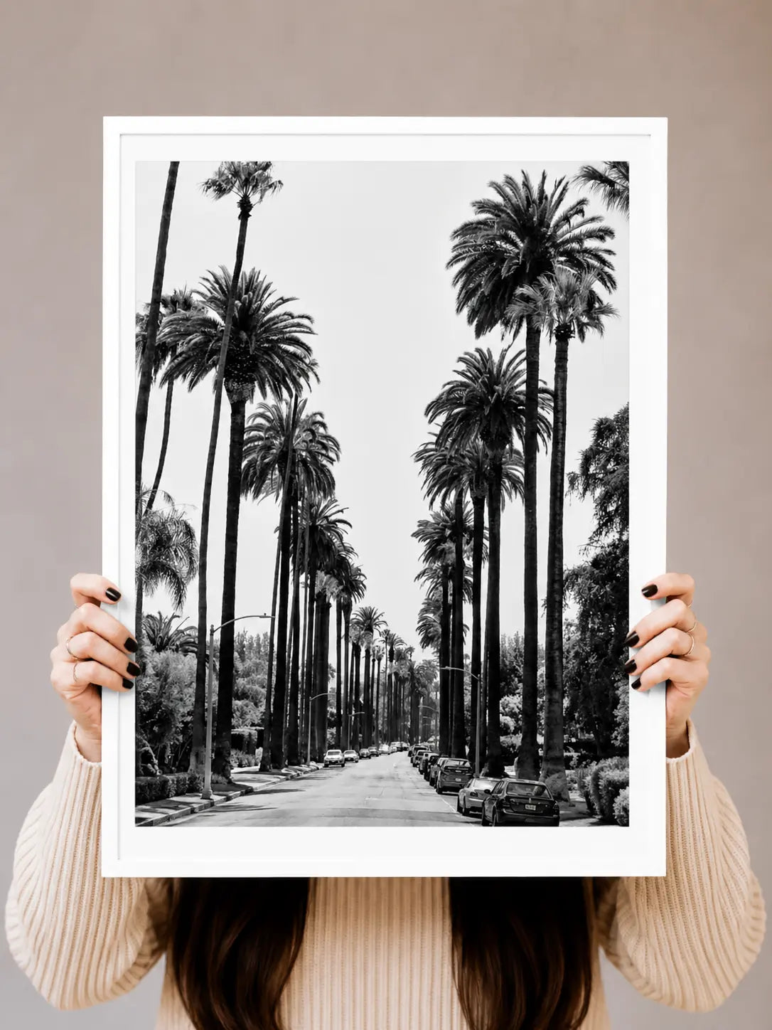Black-and-white palm tree avenue art print held up by hands in a white frame.