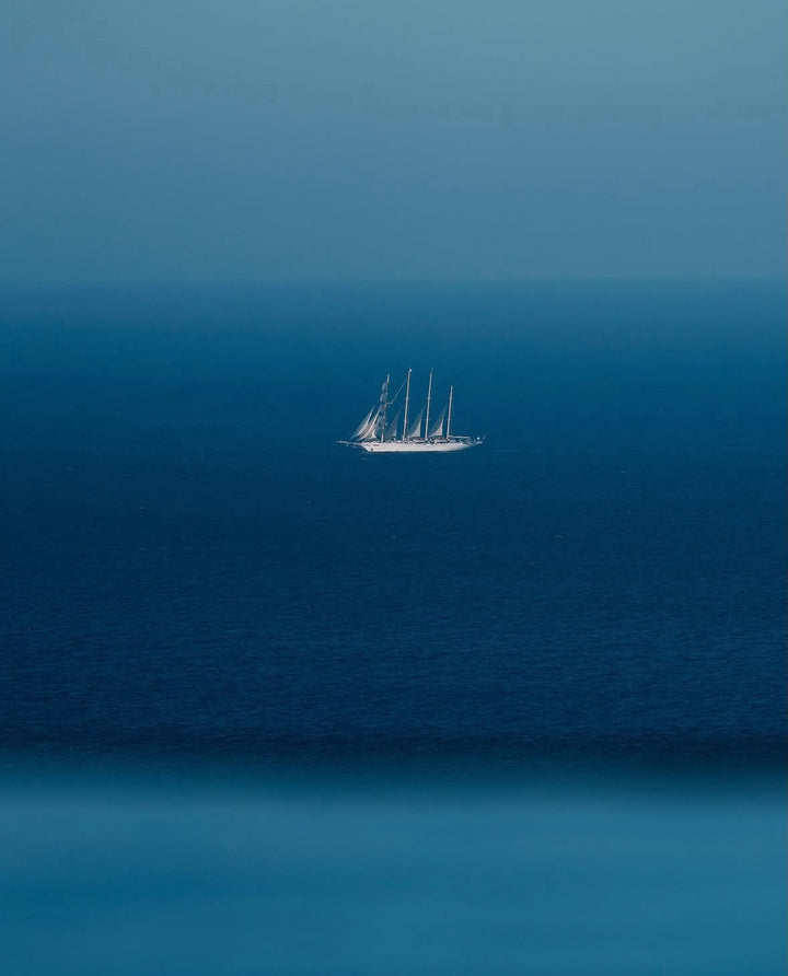 Minimalist Sailboat Print showing a small sailboat surrounded by layered shades of blue in an open seascape.