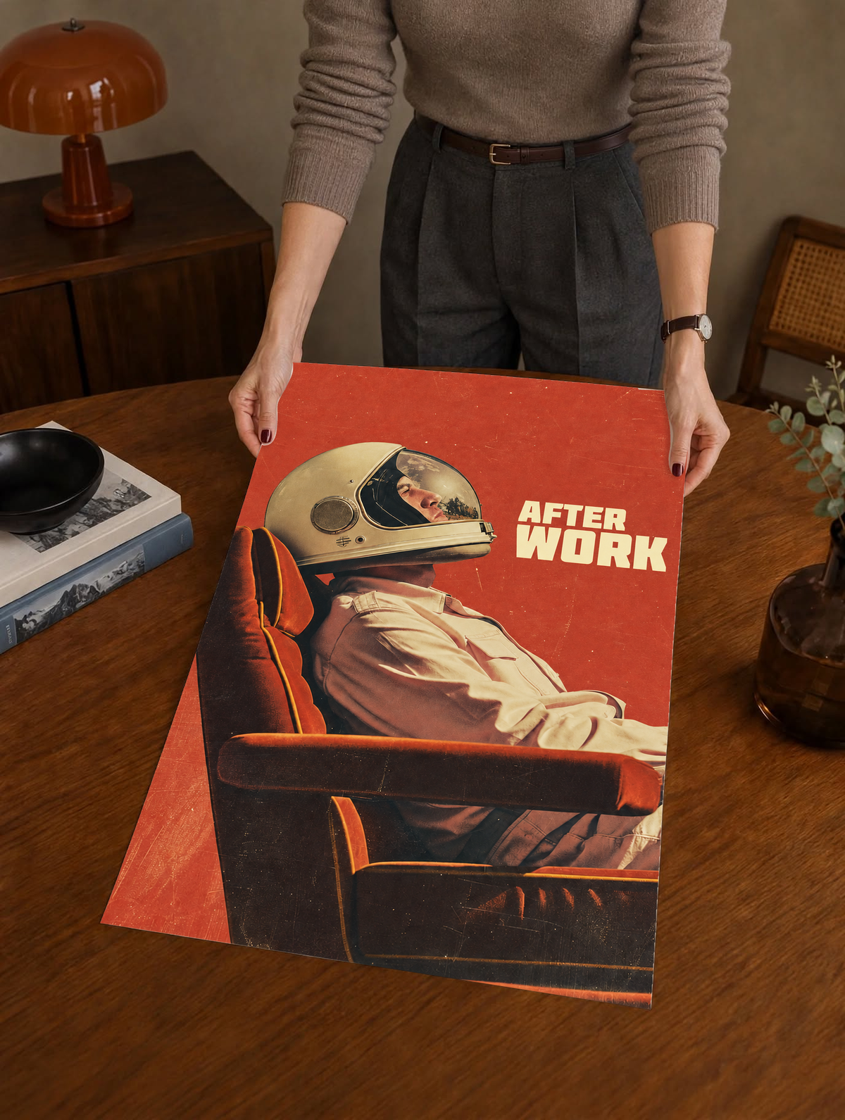 An astronaut reclining in an armchair against a burnt-orange ground as a large unframed poster held above a wooden desk