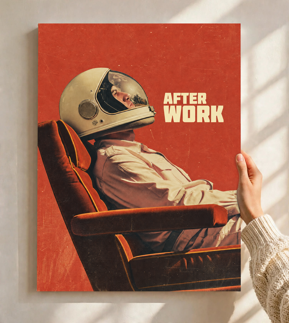 An astronaut reclining in an armchair against a burnt-orange ground as an unframed poster held against a pale sunlit wall