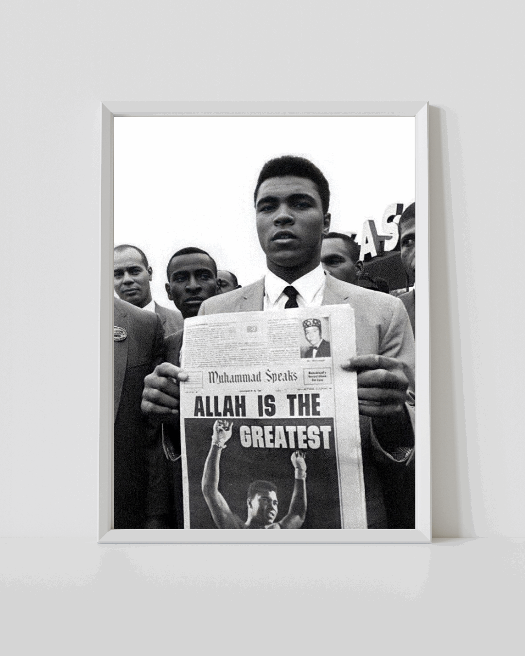 White-framed black-and-white poster of Muhammad Ali holding newspaper with 'ALLAH IS THE GREATEST'