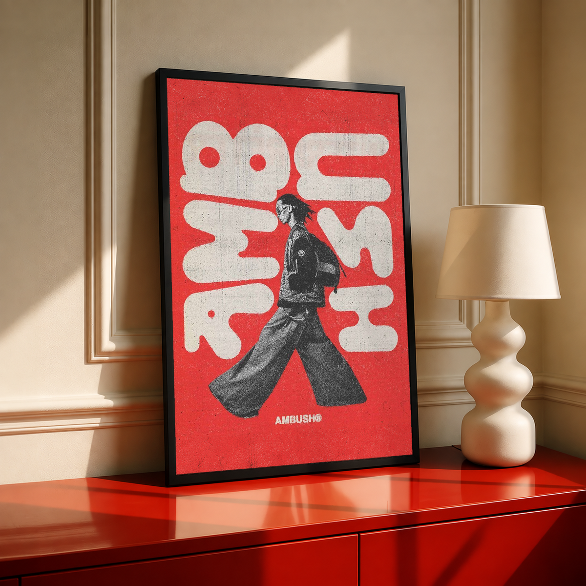 Black-framed red typography poster with a black walking figure; AMBUSH text at bottom