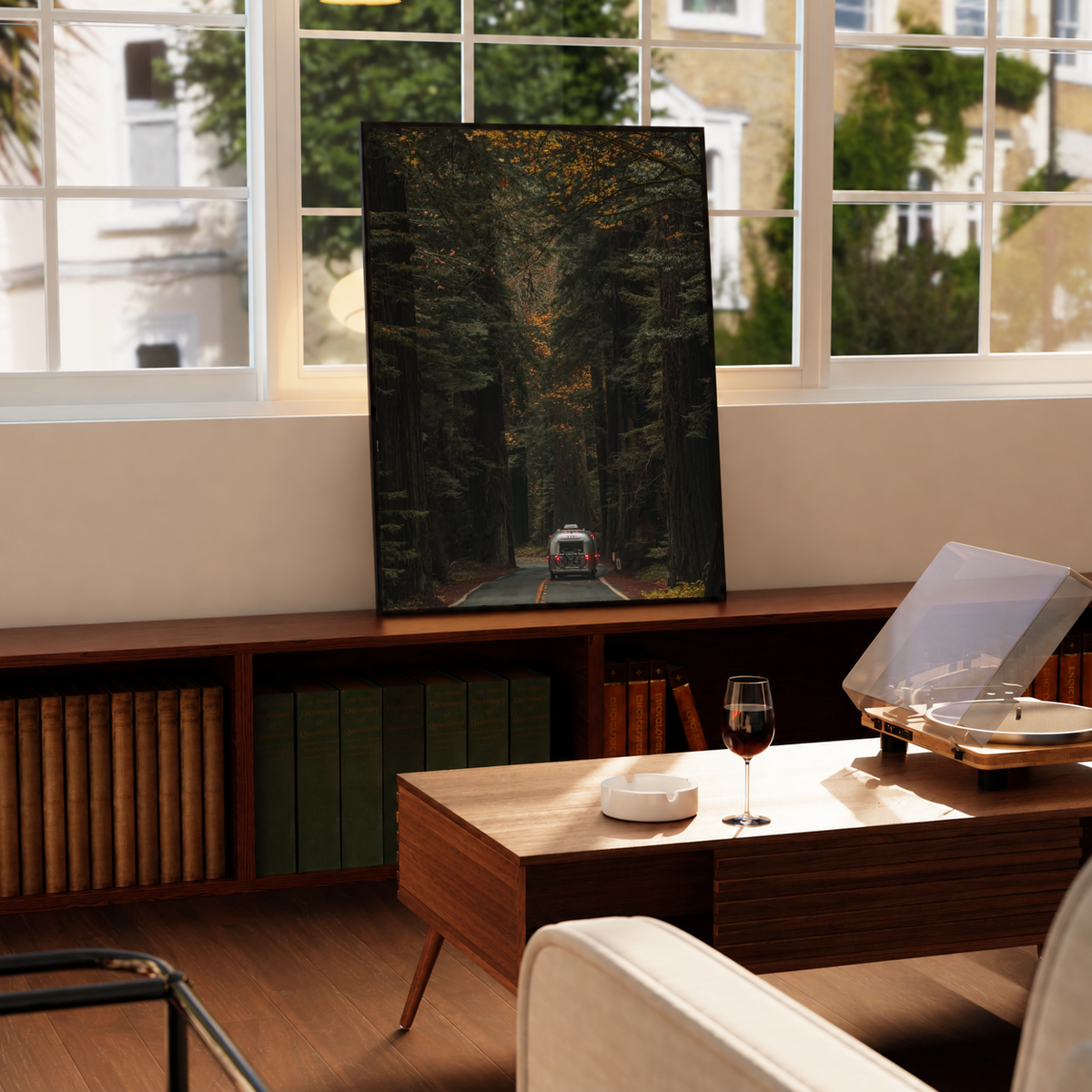 Autumn Forest Road Poster in a black frame near a window and wooden table in a sunlit sitting room.