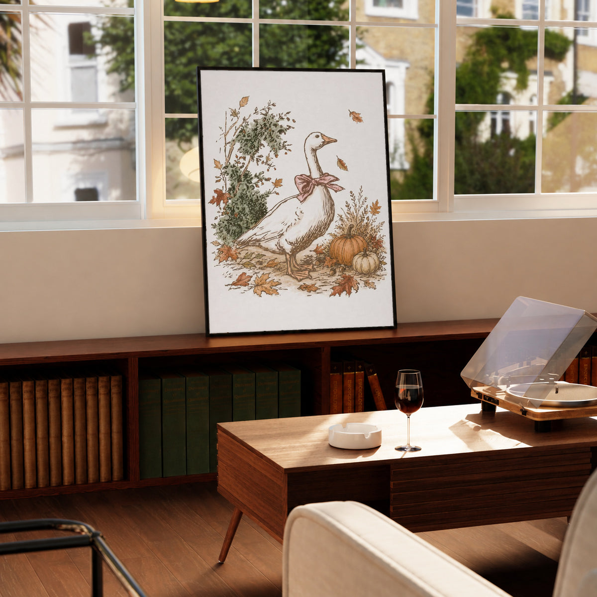 White goose with a rust pink bow among pumpkins and scattered autumn leaves in a black frame on a wooden cabinet beside a window and record player