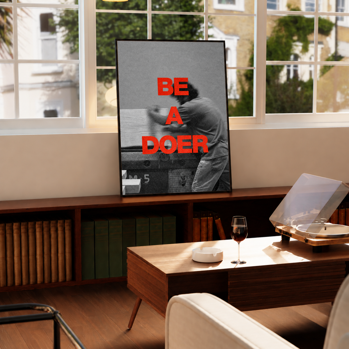 Red Be a Doer lettering over a motion-blurred monochrome figure in a black frame by a bright window above a record player