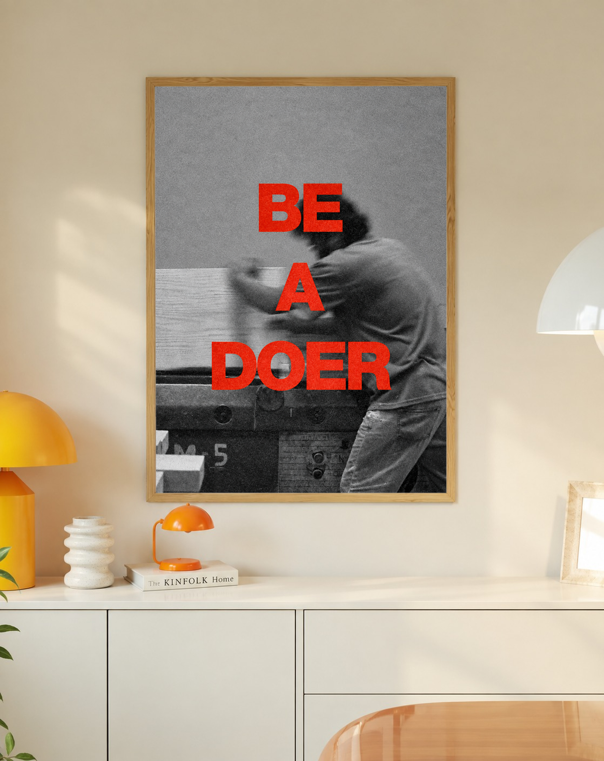 Red Be a Doer lettering over a motion-blurred monochrome figure in a slim oak frame on a cream wall above a white cabinet