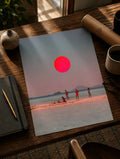 Póster costero surrealista con gran disco solar rojo sobre personas en la playa y montañas lejanas.