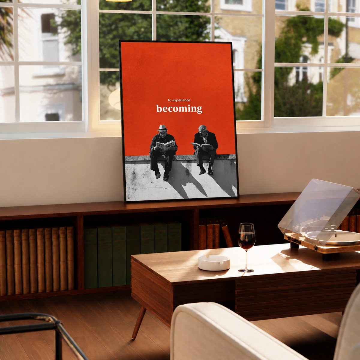 Two monochrome newspaper readers on a ledge beneath Becoming lettering on orange in a black frame by a bright window above a record player