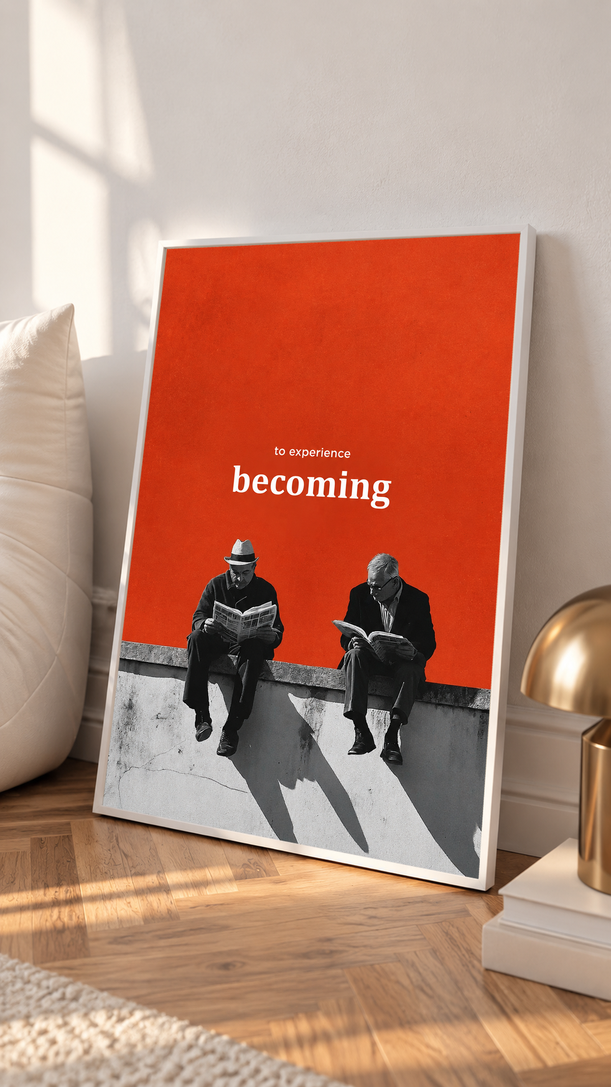 Two monochrome newspaper readers on a ledge beneath Becoming lettering on orange in a white frame on a sunlit floor beside a white cabinet