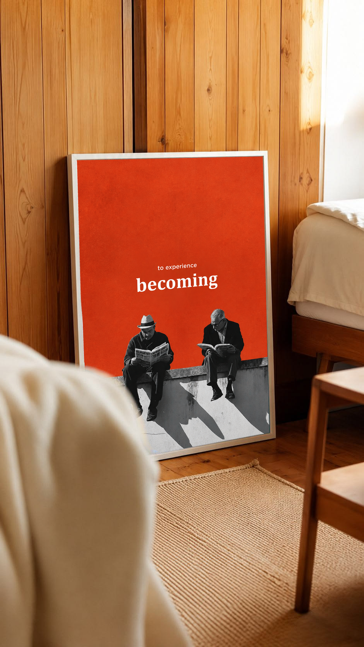 Two monochrome newspaper readers on a ledge beneath Becoming lettering on orange in a white frame leaning against warm wooden wall panels