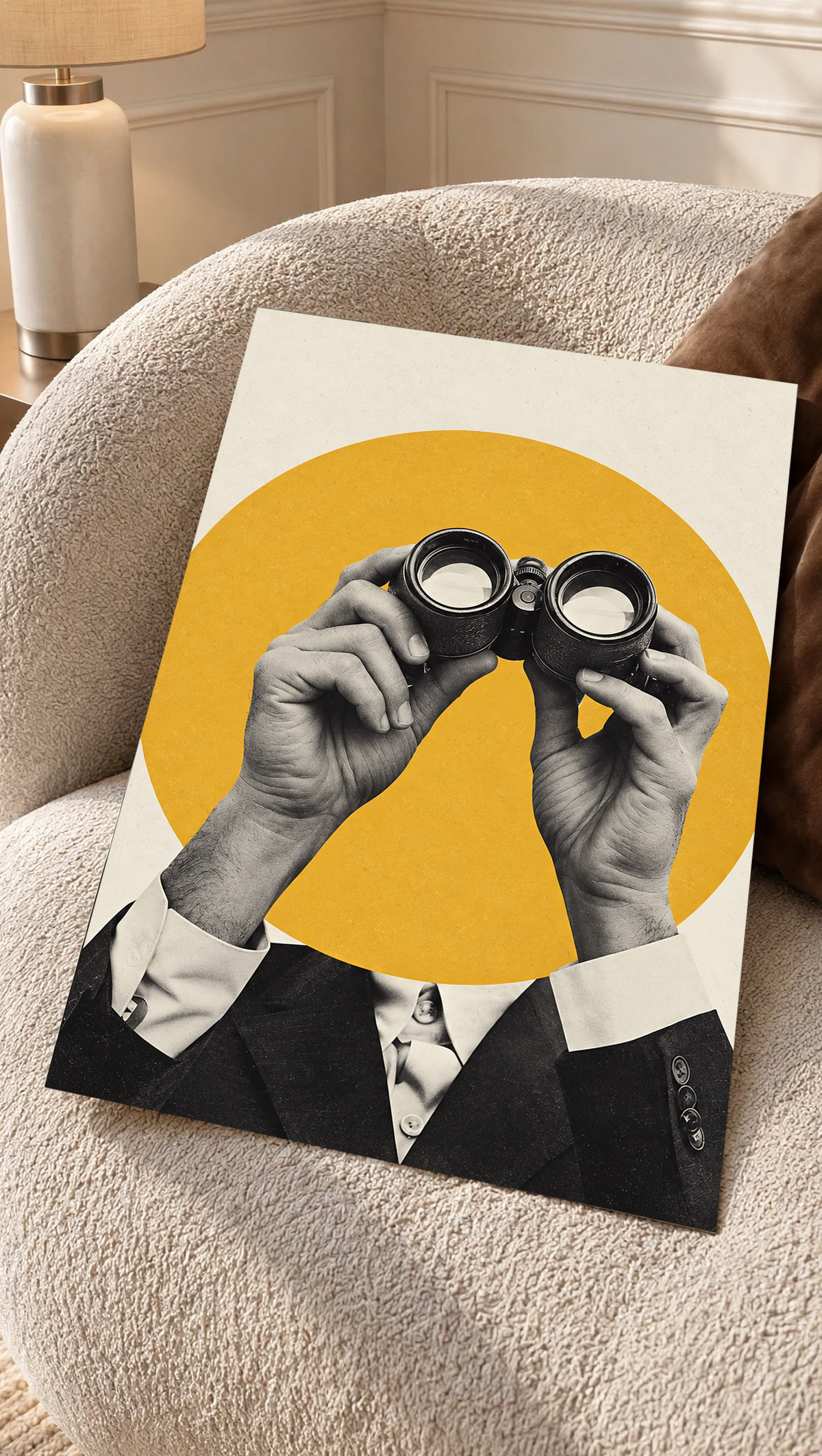 Monochrome hands holding binoculars before a mustard-yellow circle as an unframed poster resting on a cream woven chair