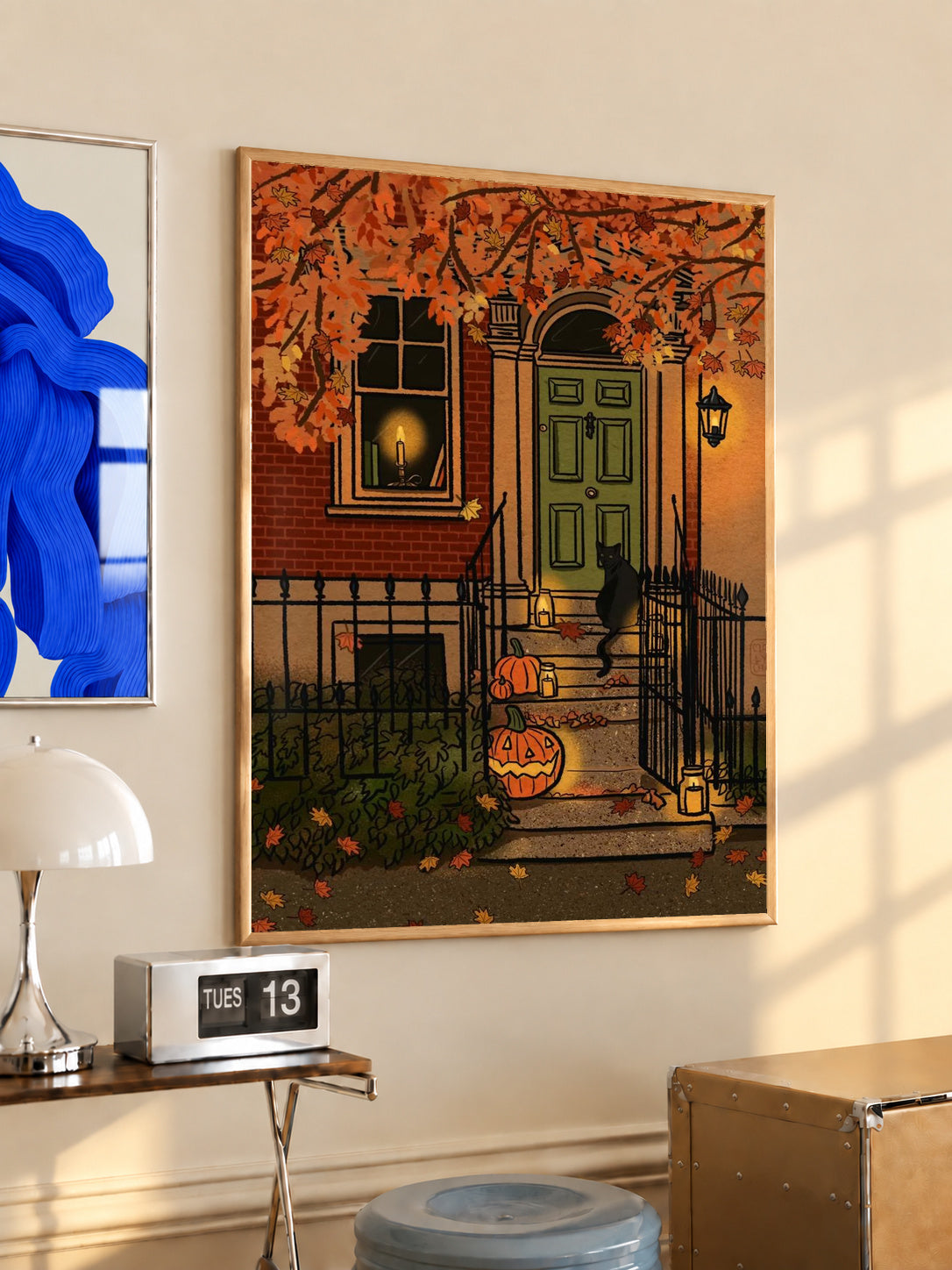 Black-framed Halloween art print on wall with green door, fence, and jack-o'-lanterns