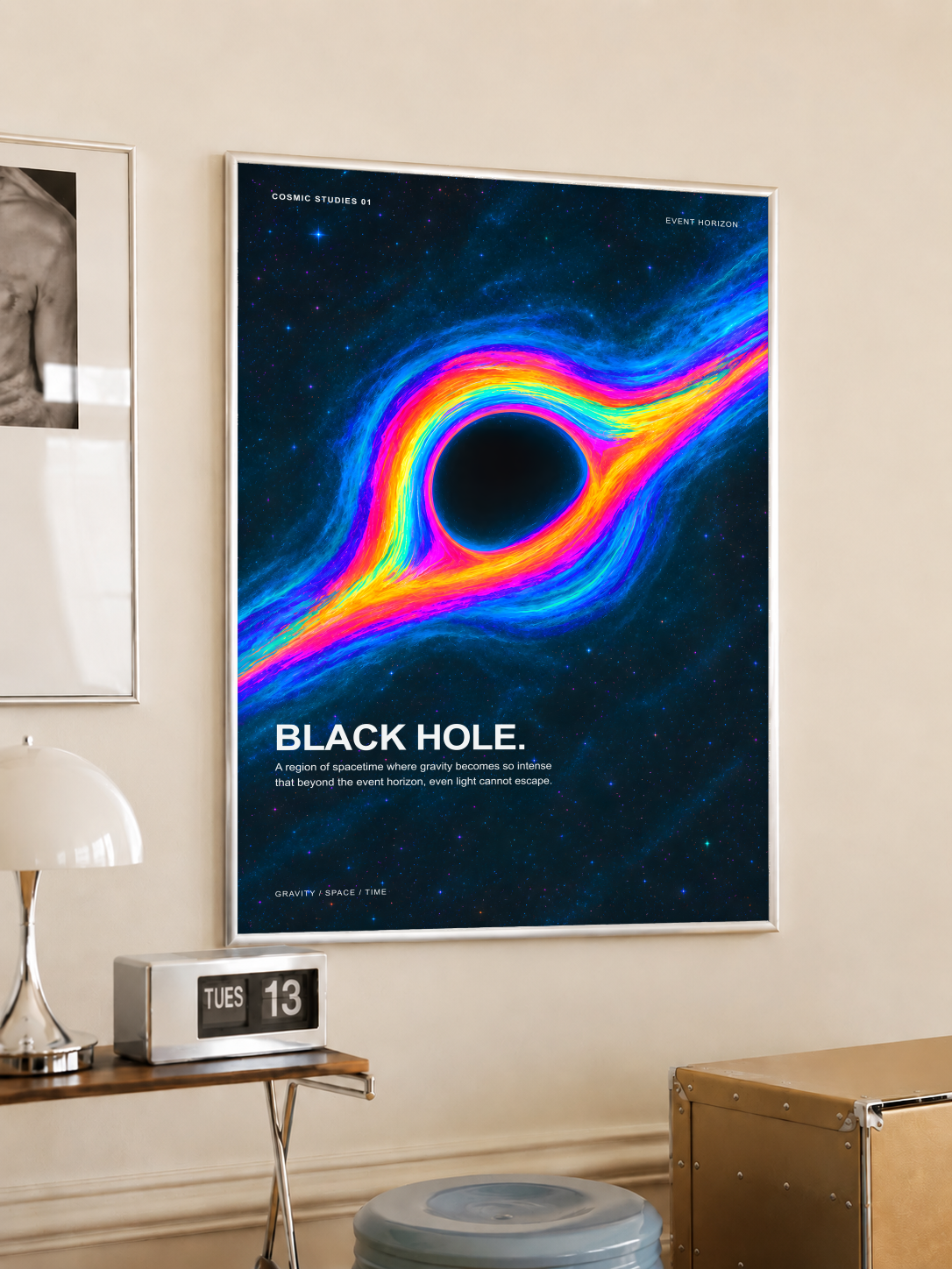 Black Hole Cosmic Studies poster with rainbow-colored accretion flow blue stars and Event Horizon labels, styled in a light frame on a cream wall beside a white dome lamp and glass side table