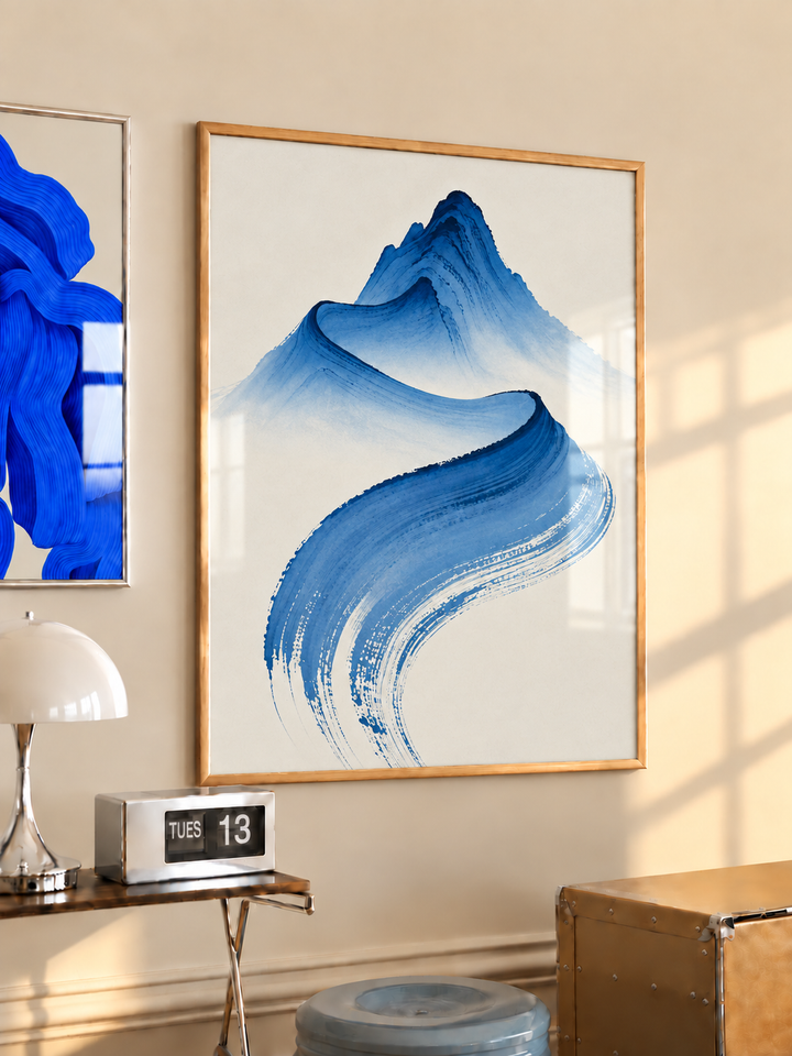 Wood-framed cobalt-blue abstract mountain brushstroke print hanging above a wooden side table in a neutral room.