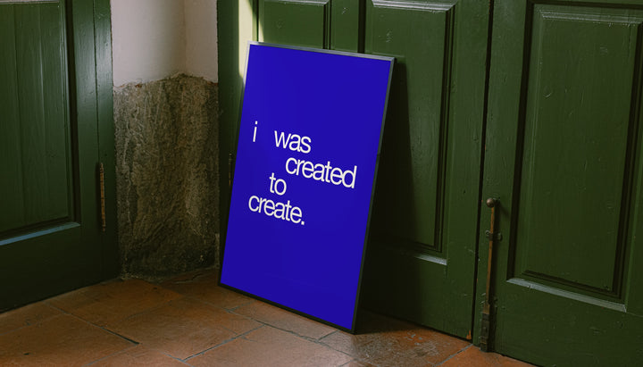 Freestanding framed blue quote typography poster with white text: “I was created to create.”