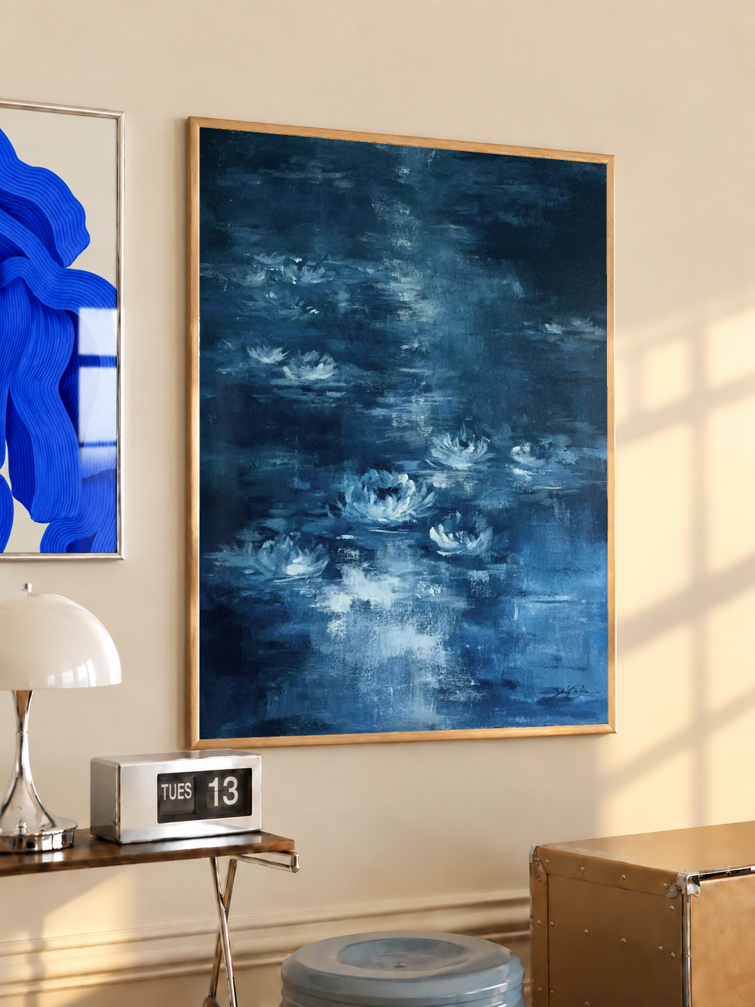 White water lilies on a blue pond in an oak frame on a warm cream wall above a small table and dome lamp
