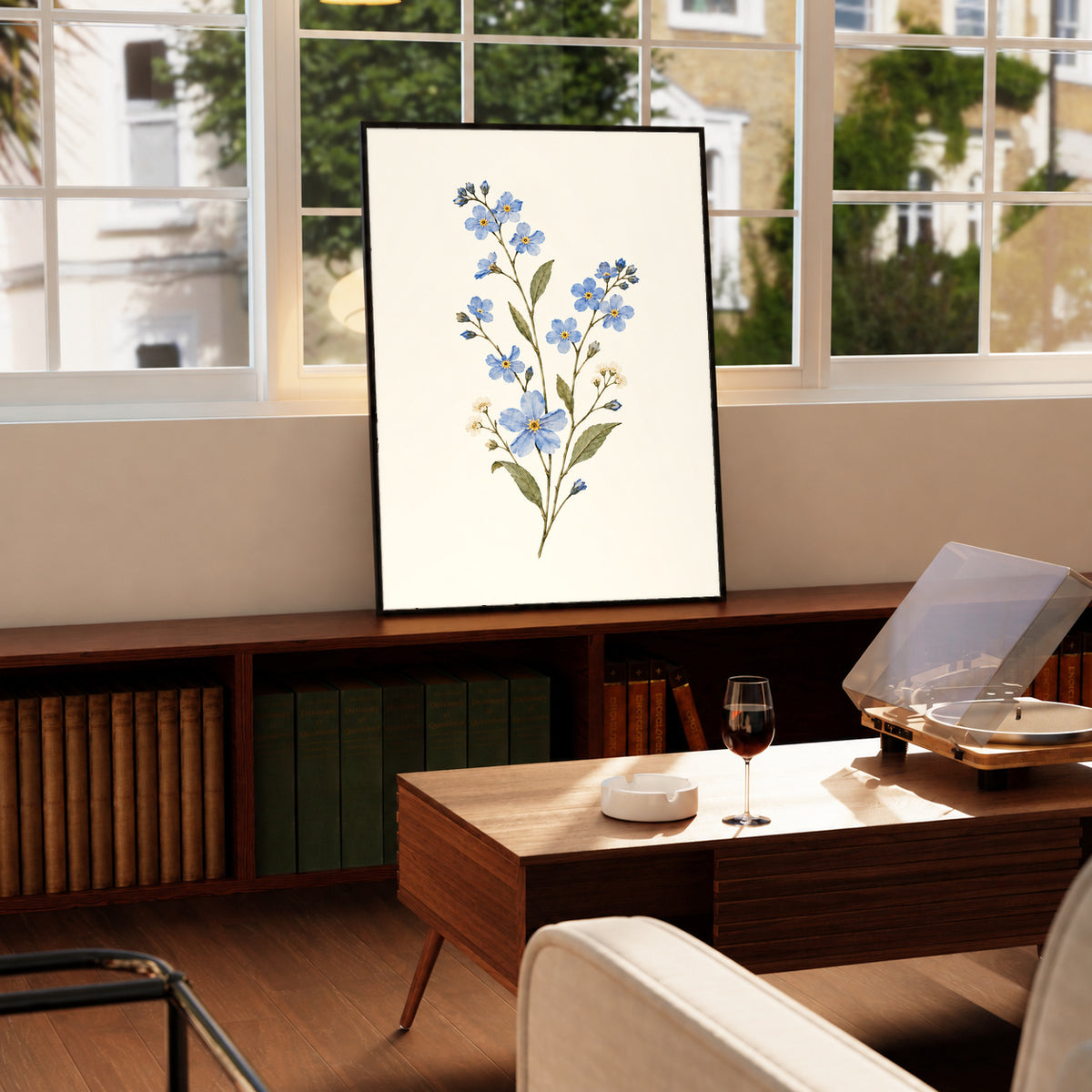 Blue wildflower sprig with small white flowers and olive green leaves in a black frame on a wooden cabinet beside a window and record player