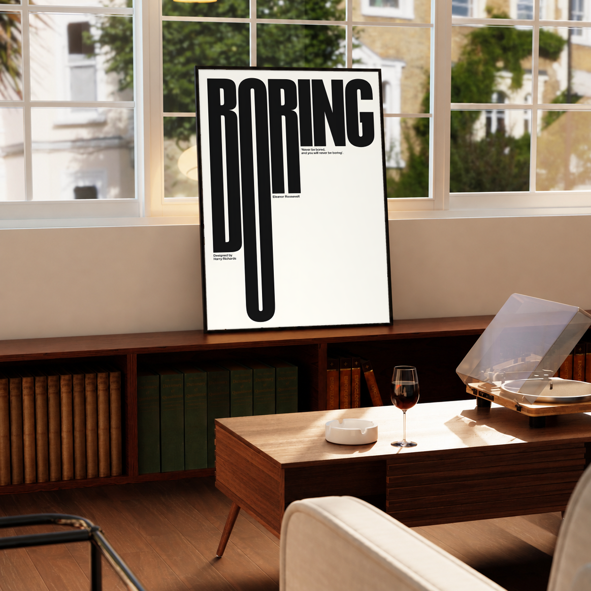 Boring typography artwork with tall black condensed letters and a small quote on cream, styled in a black frame above a wood console with books and a record player