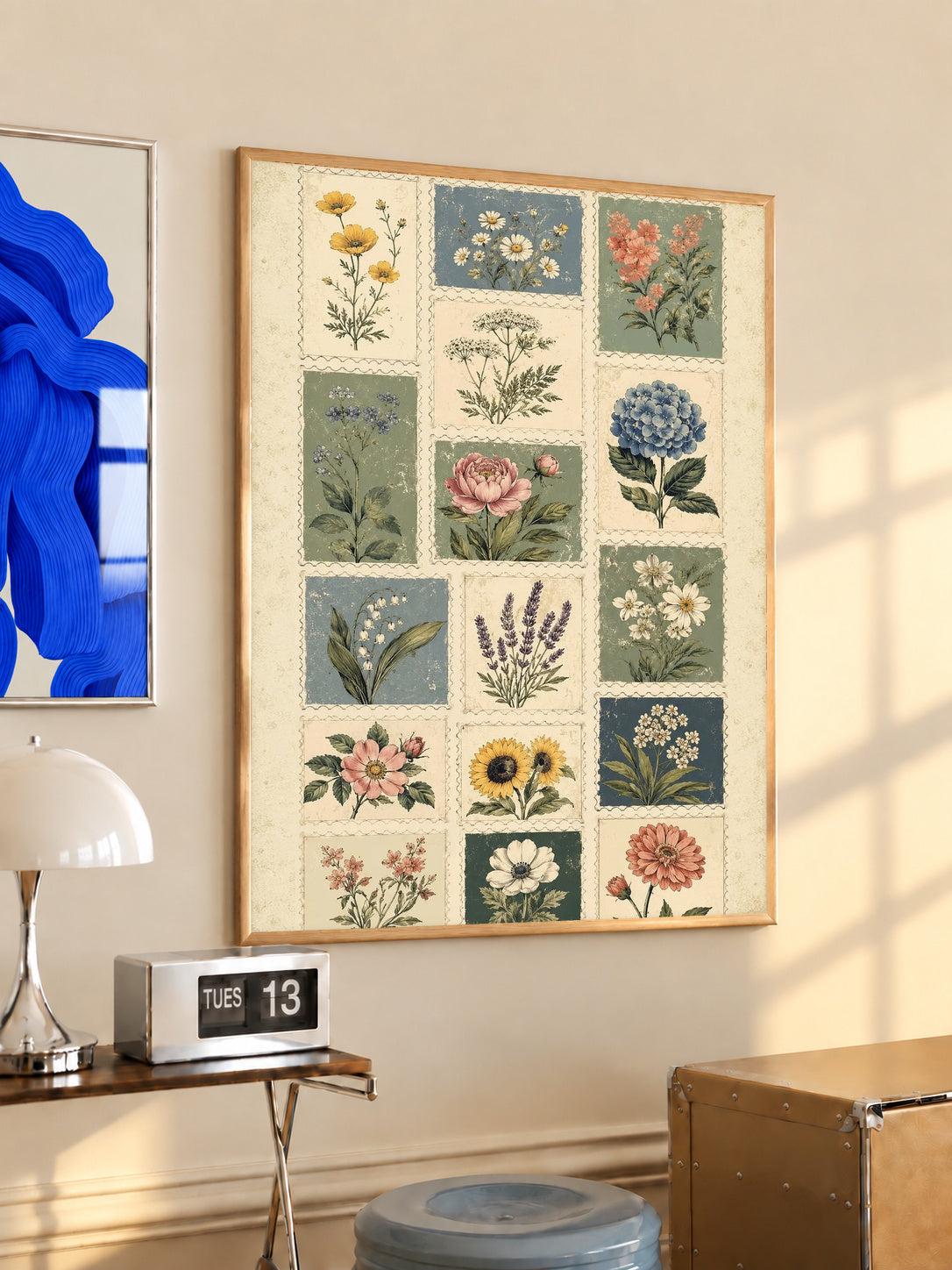 Patchwork of flower and leaf stamp style panels in sage blue pink and cream in an oak frame above a console beside a blue print and calendar
