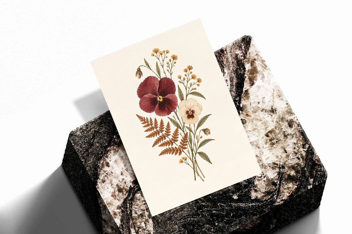 Burgundy and cream pansies with rust fern leaves and small golden flowers as an unframed print standing on a stone plinth against white