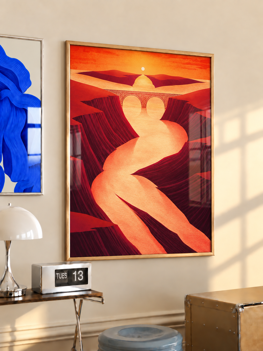Wood-framed sunset canyon and winding river bridge poster above a wooden side table with a white lamp.