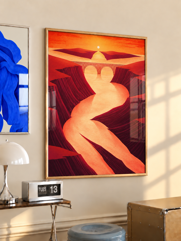 Wood-framed sunset canyon and winding river bridge poster above a wooden side table with a white lamp.