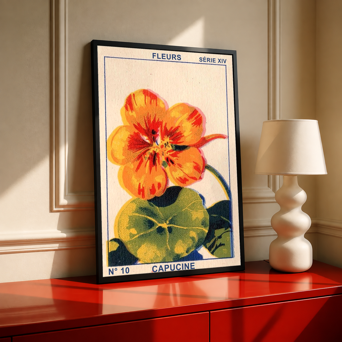 Black-framed capucine flower print with orange petals and green leaves on red table.
