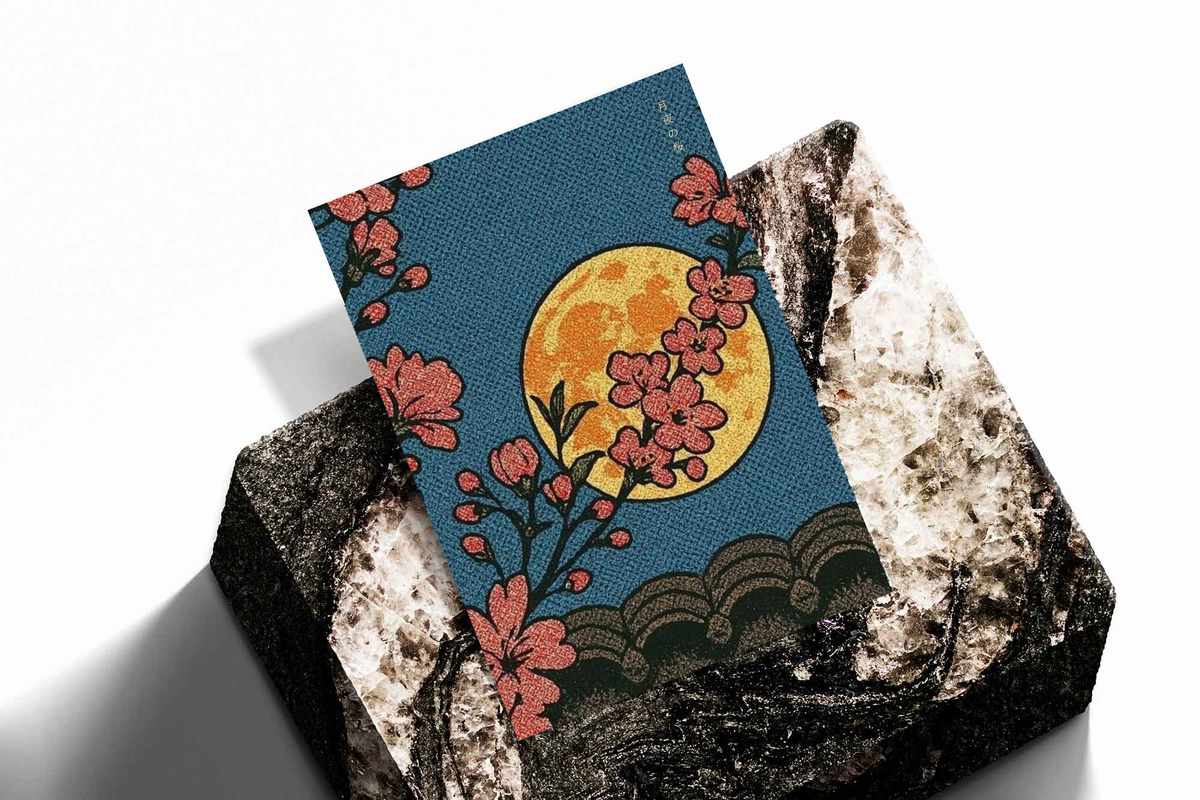 Cherry blossoms, yellow moon and patterned waves as an unframed print propped against a pale wall on a rough stone